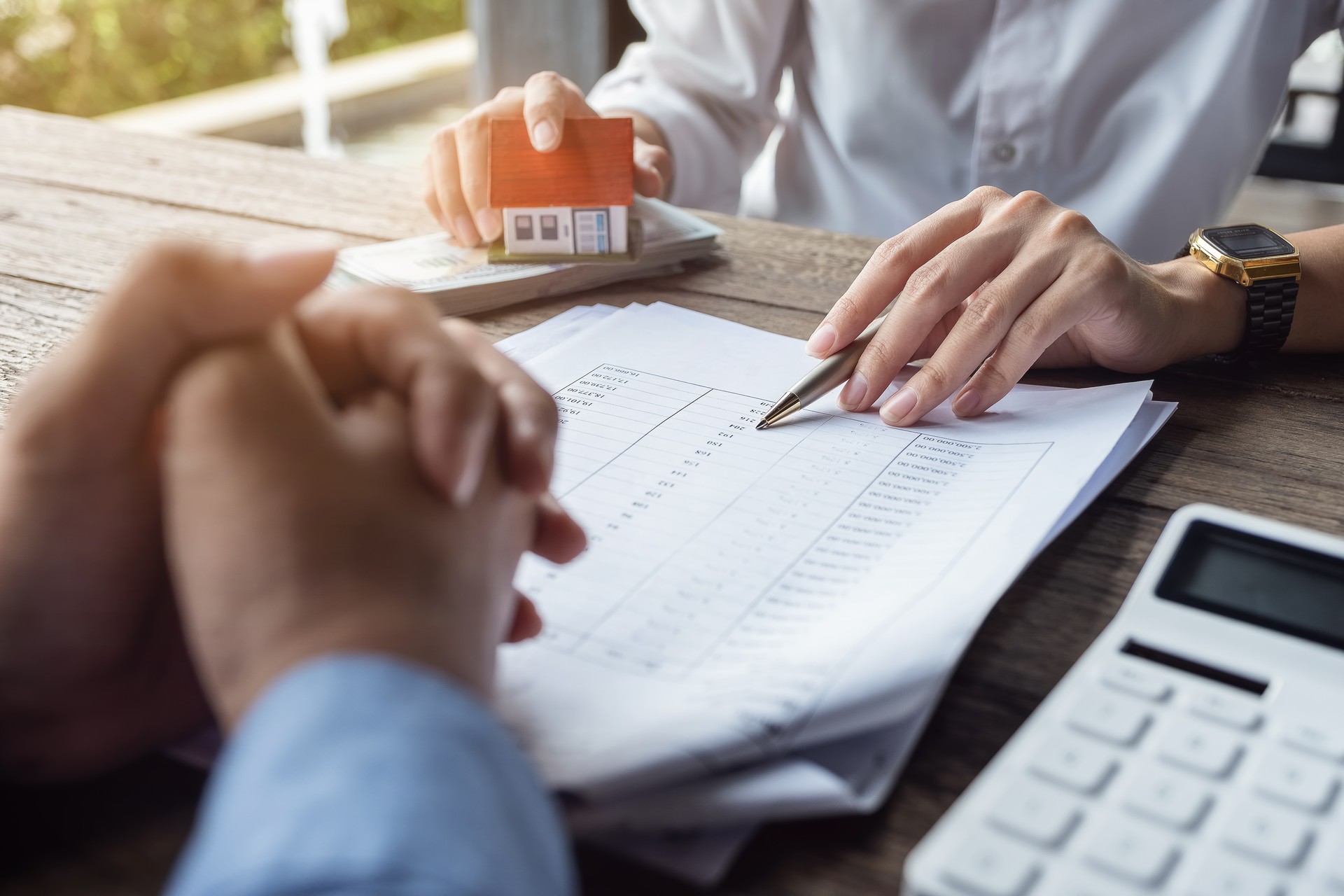 Loan agreement, real estate agent or bank officer describes the loan interest to the customer, along with loan documents with a home-style pen and a replica money on a wooden table.