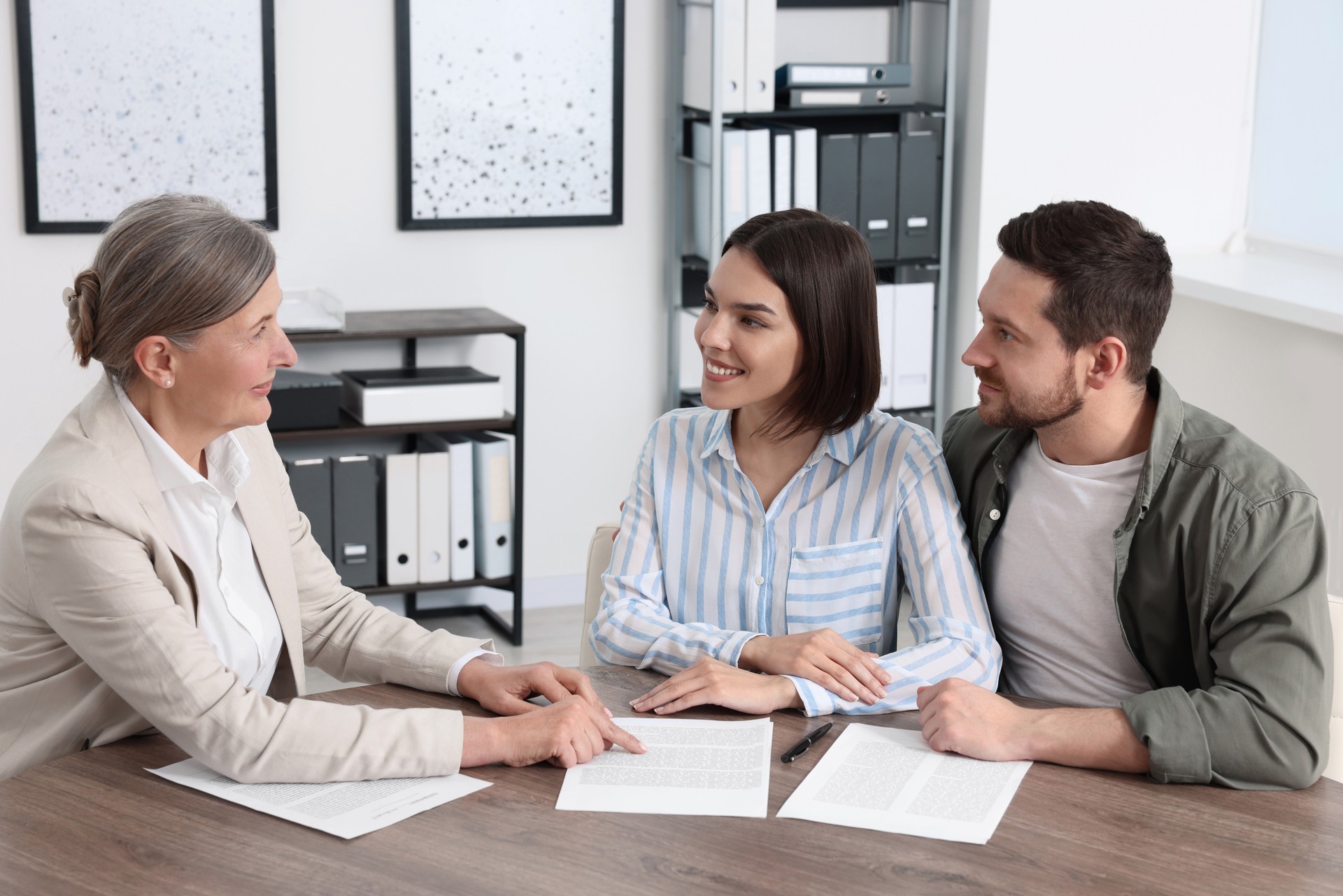 Young couple consulting insurance agent about pension plan at wooden table indoors